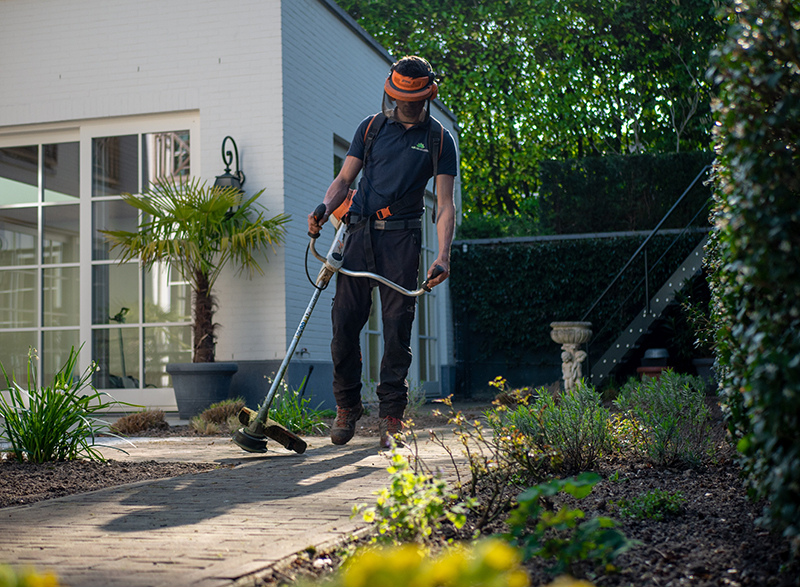 Mann mit Freischneider und Schutzkleidung im Garten 